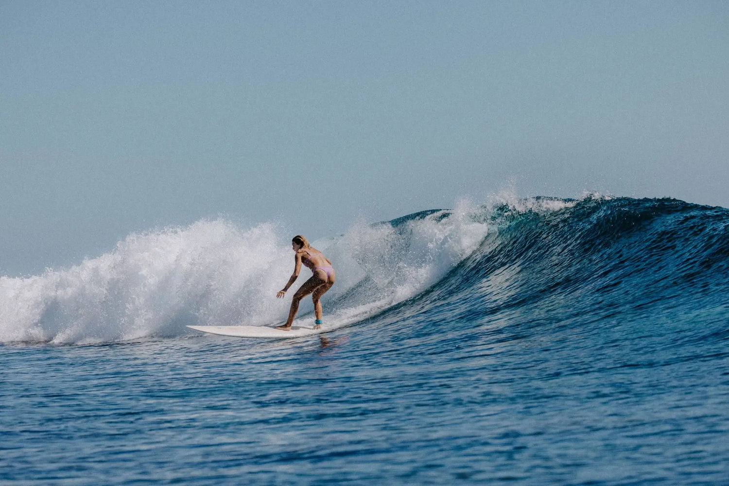 Woman surfing wearing our Tau Swim Bottom and Bindi Top in Lavender