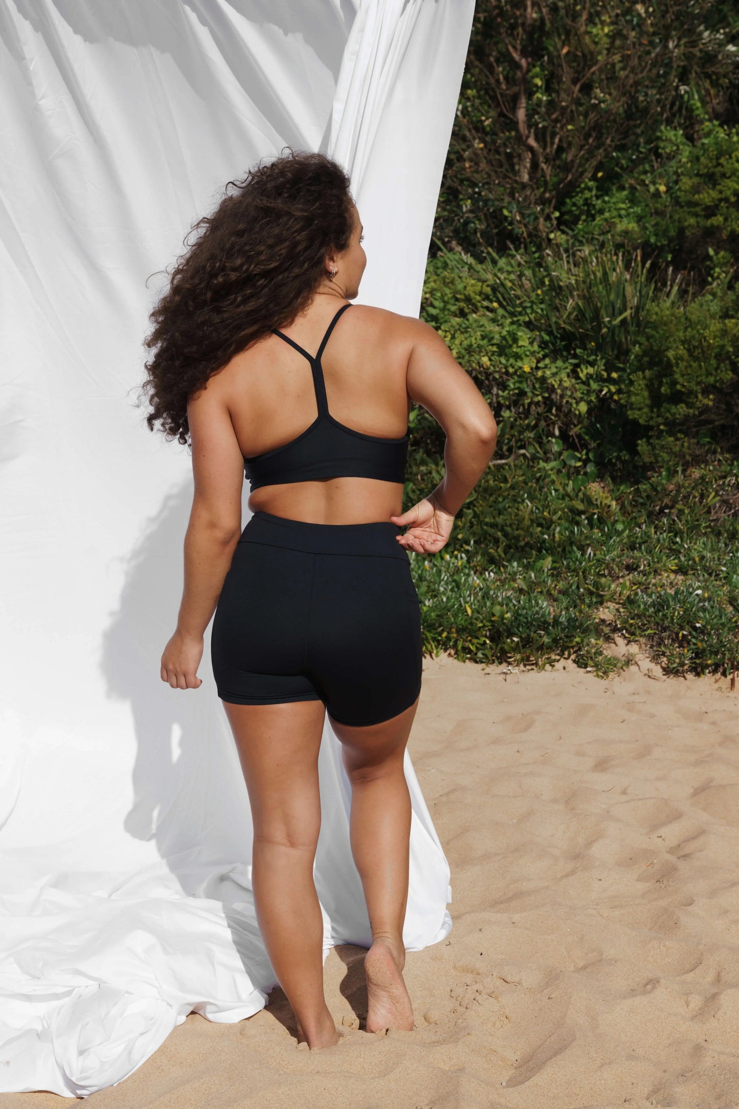 Model at the beach facing the back wearing our Inala Crop and Allawah Shorts in the colour Black